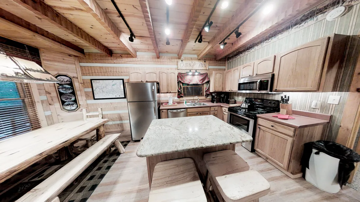 A close-up view of the kitchen and dining zone, featuring a granite island countertop, a large wooden dining table, stainless steel appliances, and warm wooden cabinetry. The setup is ideal for cooking together, sharing festive dinners, or gathering for breakfast.