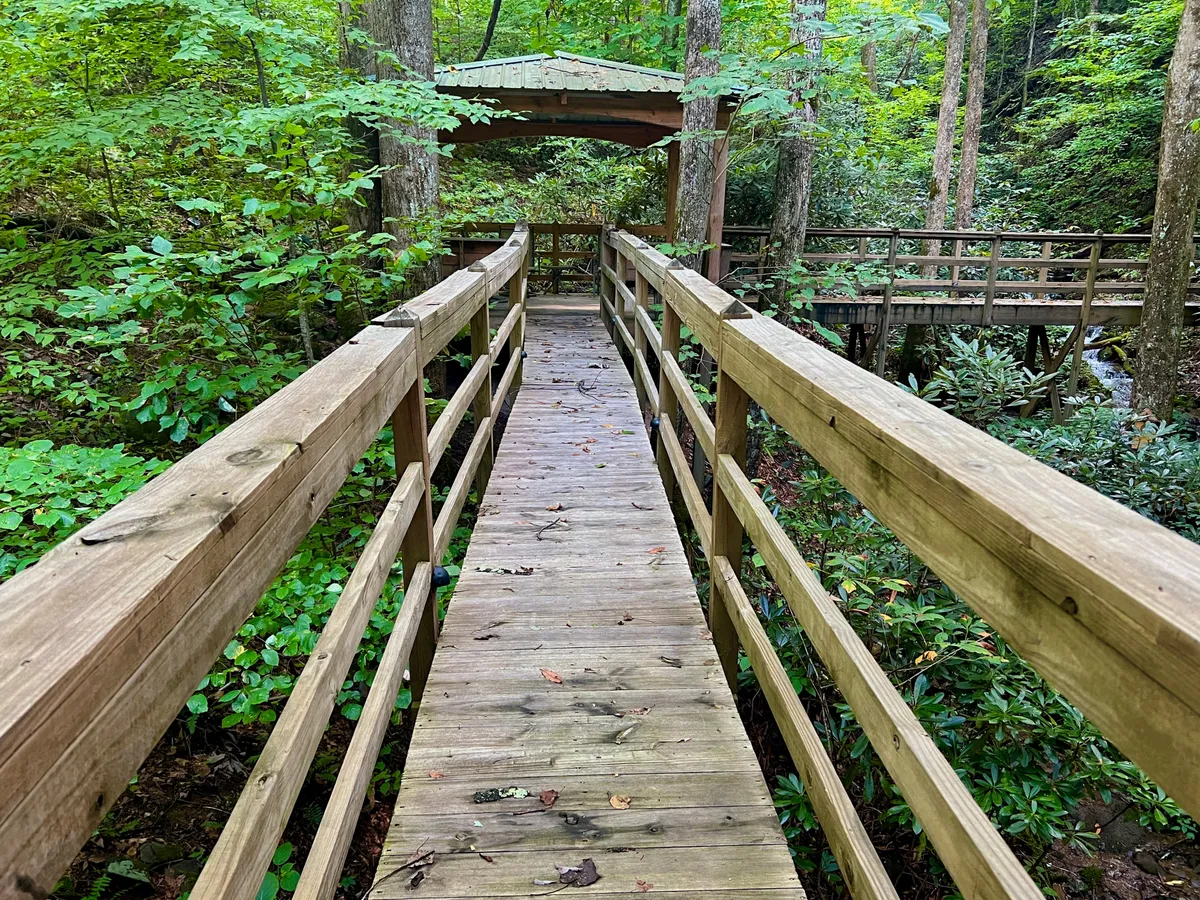A peaceful exterior view showing a wooden walkway leading to a gazebo, surrounded by lush greenery. The gazebo is inviting for gatherings, with space for a grill and outdoor seating, perfectly attuned to alfresco dining and socializing with the sounds of nature nearby.
