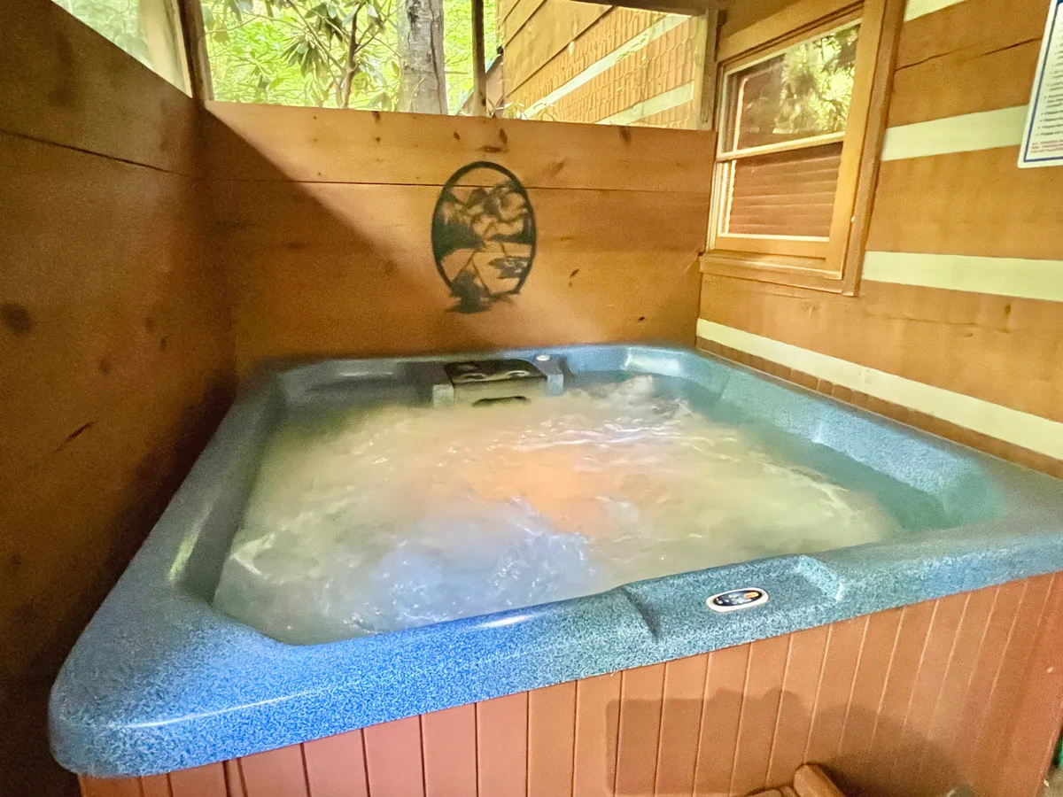 A tranquil scene featuring a hot tub nestled within wooden walls, with natural light filtering in from a nearby window. The soothing setting creates a sense of privacy and comfort, perfect for unwinding after a day of mountain adventures.