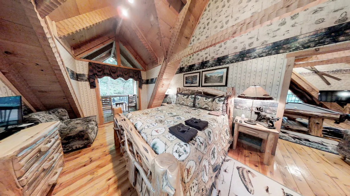 This image features a king-sized bed with patterned bedding, wooden furniture, and large windows allowing natural light to flood the room. The view outside offers glimpses of the surrounding nature, while the warm, inviting décor creates a restful retreat.