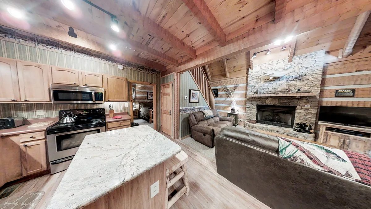 A warm, inviting living space with a spacious kitchen island, cozy fireplace, comfortable sofa, and rustic wooden beams. The room is designed for entertaining guests, relaxing by the fire, and gathering for group activities like game nights.