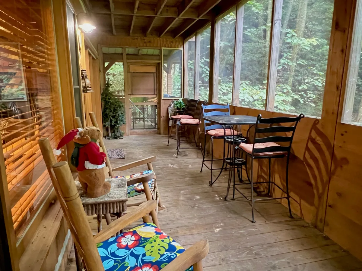 A tranquil corner featuring a classic wooden rocking chair with colorful cushions, bar stools, and a view of greenery outside. The space feels connected to nature, perfect for unwinding after a game night.