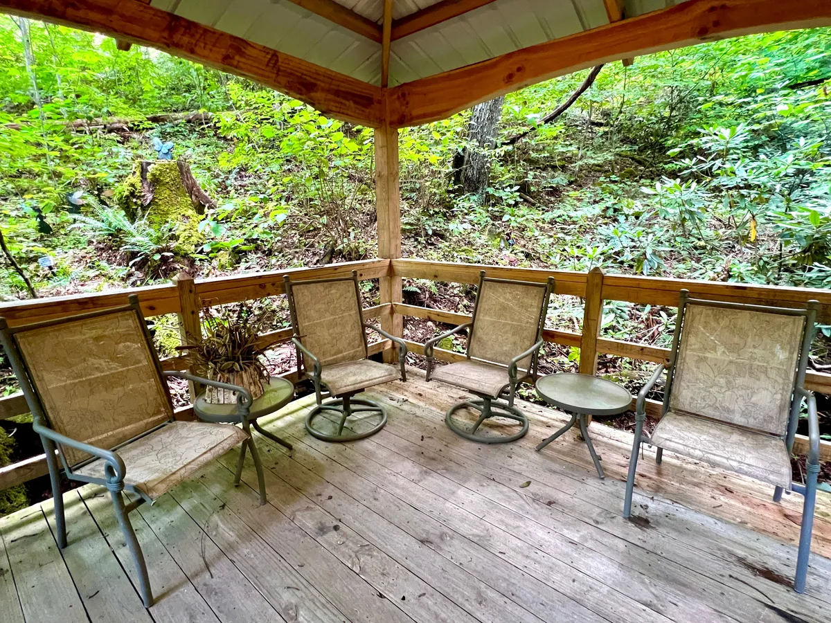 A spacious wooden deck surrounded by greenery, featuring a comfortable seating arrangement ideal for relaxing, socializing, or enjoying peaceful views. The scene is serene and immersed in nature, inviting sunrise coffees or sunset toasts as described in the section.